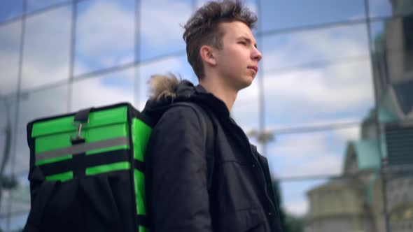 Delivery Man with Green Bagpack Walks Through the City with Food Delivery