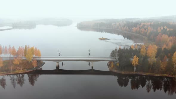 Aerial, tilt down, drone shot, flying towards a car on a bridge, surrounded by mist and autumn color