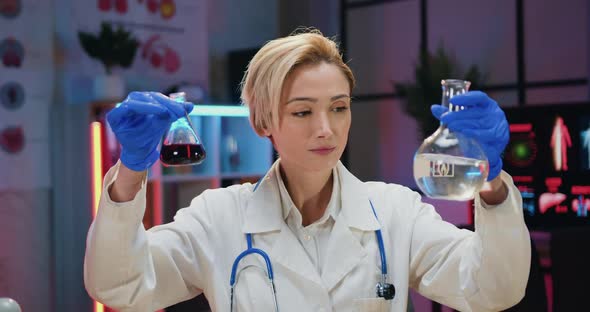 Woman Chemist in Uniform and Gloves Conducting Chemical Researches in Glass Flasks in Evening Lab