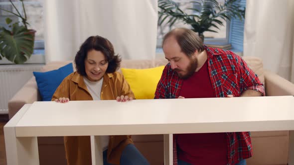 Adult Son Helping Aged Mother Assembling Wooden Shelf at Home