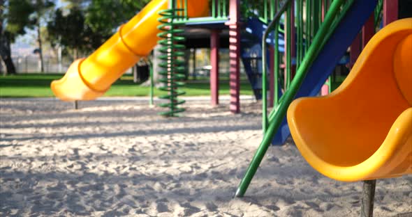 Slide right across a yellow slide in an empty kids park playground with equipment and a jungle gym.