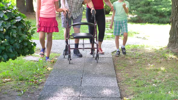 young caregiver accompanies with the grandchildren an elderly gentleman helping him to walk