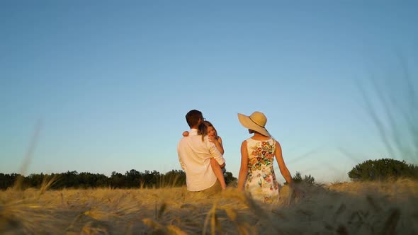 Tired Child on Hands of Father in Wheat Field at Sunset