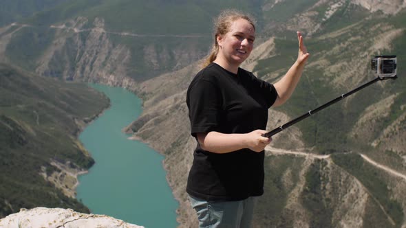 A girl in a black T-shirt drinking water from a plastic bottle against a background of mountains