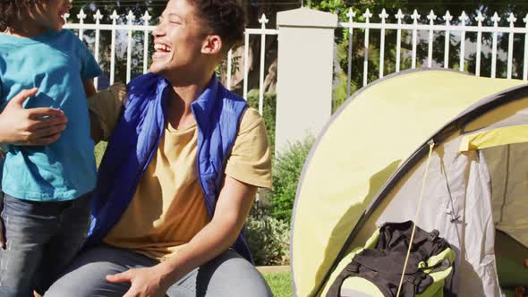 Happy biracial man and his son building tent together in garden