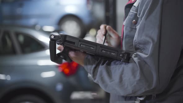 Side View of Unrecognizable Male Auto Mechanic Working with Equipment in Repair Shop. Caucasian Man