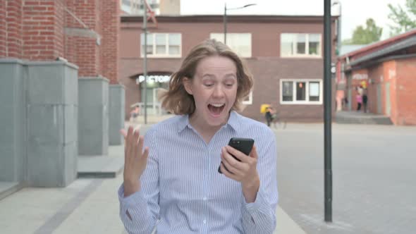 Woman Celebrating Success on Smartphone While Walking in Street