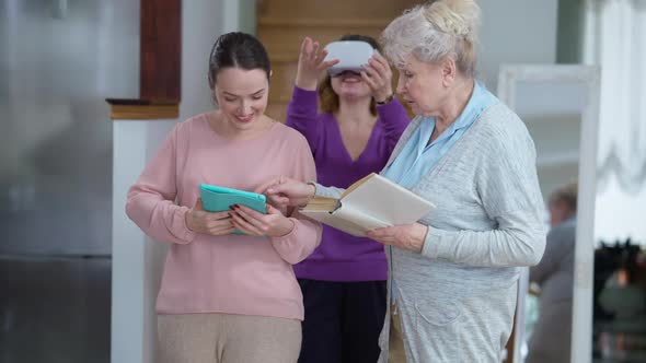 Smiling Positive Senior Grandmother with Book and Young Granddaughter with Tablet Talking As