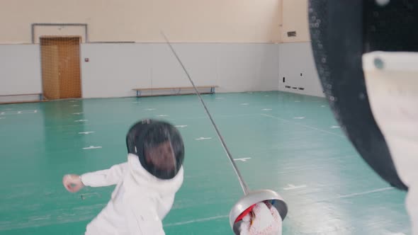 Two Young Women in White Protective Suits Having a Fencing Training in the Gym - One Woman Attack