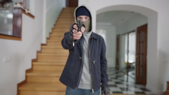 Blurred Masked Male Criminal Aiming Gun at Camera Indoors