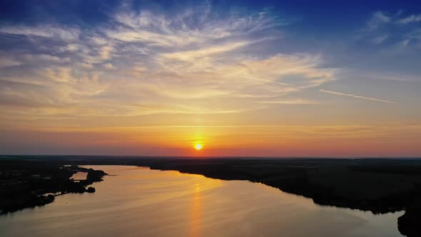 Amazing orange sunset over the river. Magic aerial view of evening sun among clouds.