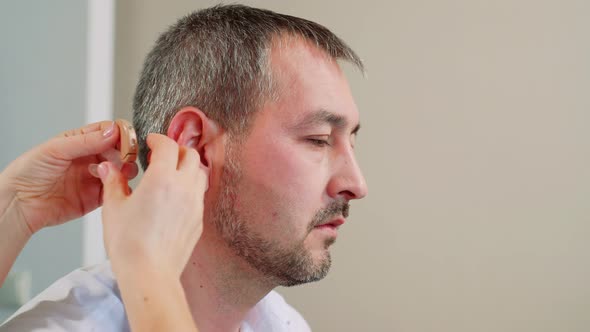 Woman Doctor Puts a Hearing Aid on A Man.