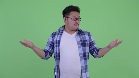 Happy Young Overweight Asian Hipster Man Comparing Something