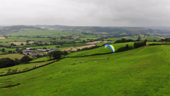 Aerial shot of a Paraglider coming into land with the English countryside behind