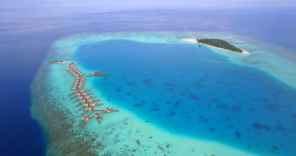 Aerial drone view of scenic tropical island and resort hotel with overwater bungalows in Maldives.