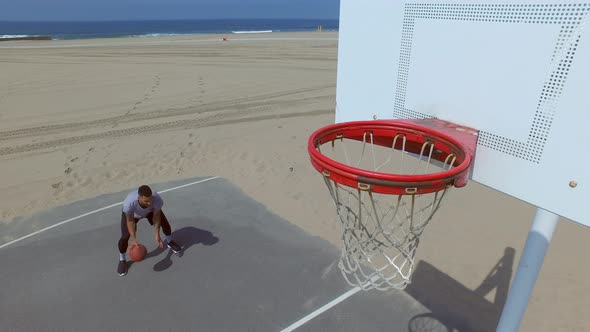 A man takes a layup shot while playing one-on-one basketball hoops on a beach court.