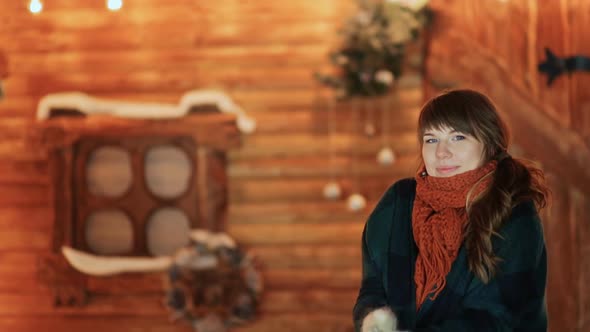 A Frozen Girl in Mittens Warms Herself on the Background of a Wooden Fairytale House