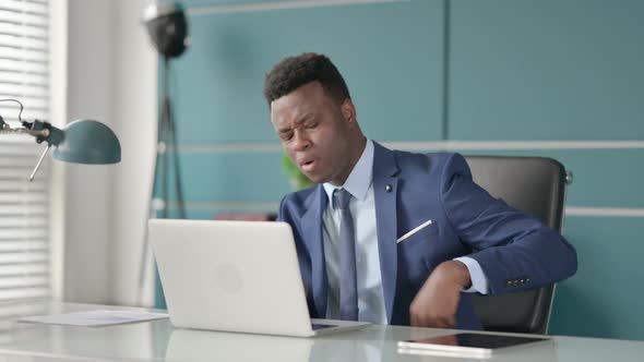 African Businessman Having Back Pain While Using Laptop in Office