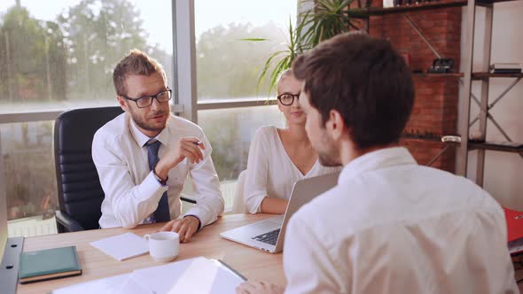 Caucasian Male Boss with Glasses and Light Bristle Sitting at Table with Female Secretary