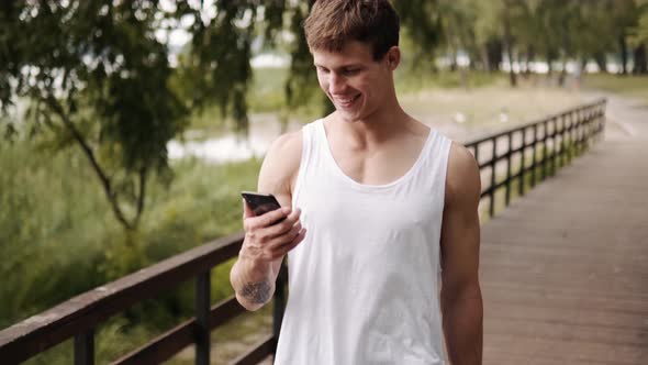 A sporty guy is using his mobile walking on the bridge