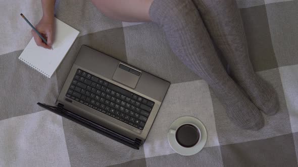 Overhead Shot, Young Business Girl Working Using Laptop and Notepad Sitting on the Bed at Home