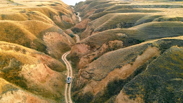 Above View of White Crossover Riding Winding Country Road Through Hills Up to Sea at Daytime