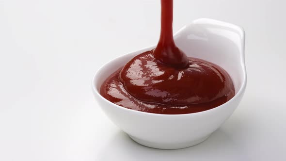 Pouring ketchup in bowl on white background