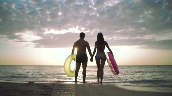 Silhouette of Young Couple on the Beach with Rubber Rings During Sunset