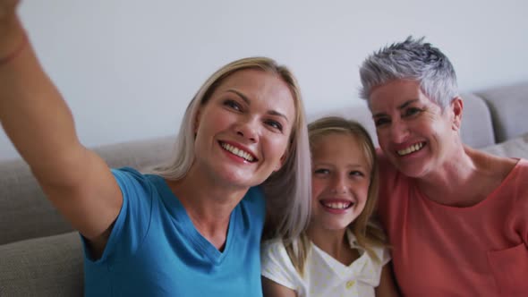 Caucasian grandmother, mother and daughter smiling while taking a selfie with smartphone at home