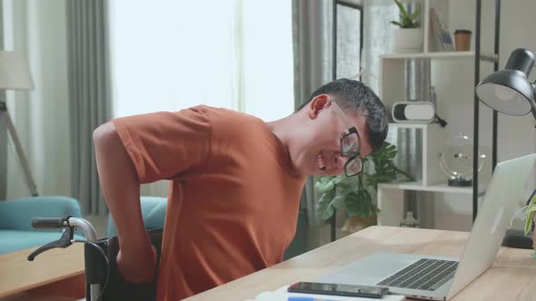 Young Asian Boy Sitting In A Wheelchair Using Laptop Computer And Pain His Back At Home