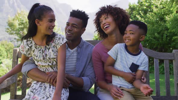 Happy african american parents, daughter and son sitting outdoors on bench