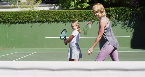 Caucasian mother teaching her daughter to play tennis at tennis court on a bright sunny day