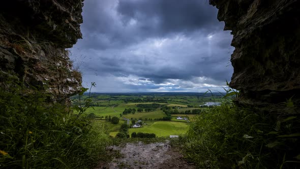 Time lapse of rural farming landscape with grass fields and hills during a dark cloudy day viewed fr