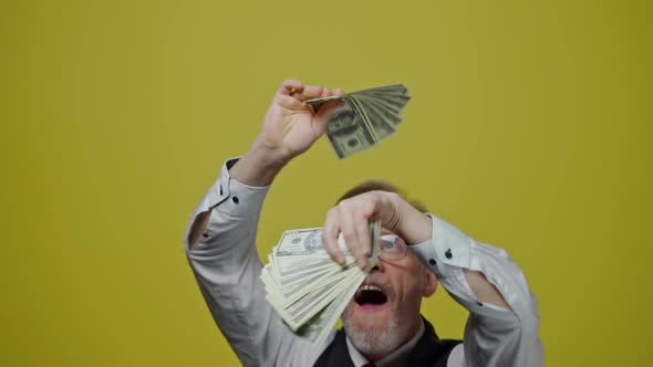 Good-looking joyful man with money on yellow background. Satisfied modern gray-bearded grandfather p