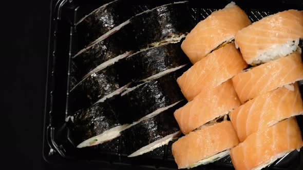 Vertical Video. Sushi Rolls Rotates in a Plastic Container on a Black Background