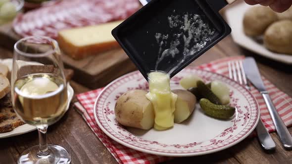 Putting melted raclette cheese on freshly boiled potatoes, swiss cuisine