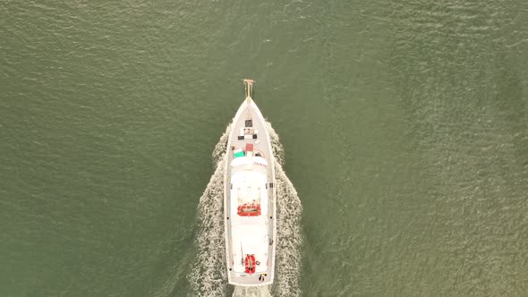 A top down drone shot directly above a fishing boat heading out to sea on a cloudy morning. The dron