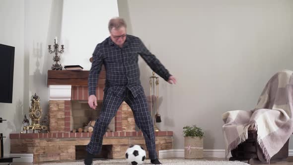 Wide Shot of Happy Active Caucasian Retiree Training with Football Ball Indoors. Positive Healthy