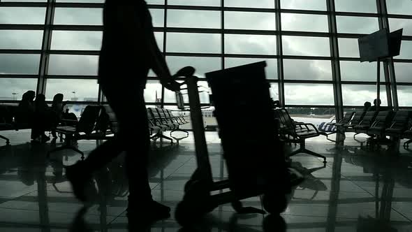 Travelers Walking Along Window in Airport Terminal, People Silhouettes Walking.