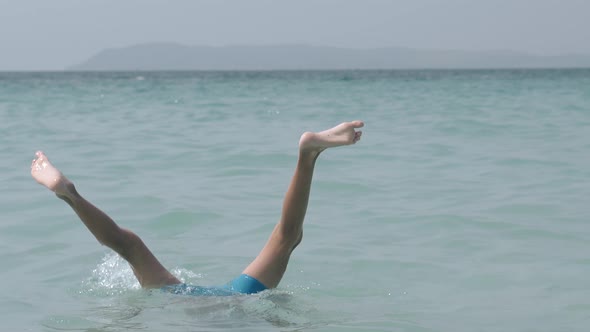 Blonde Boy in Swimming Trunks Dives Into Water Upside Down