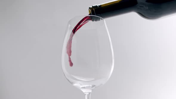Pouring Red Wine Into a Clear Glass on a White Background in Slow Motion