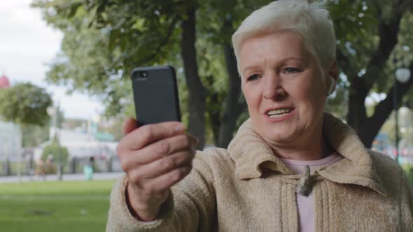 Confident Senior Caucasian Woman Grandma with Modern Wireless Headphones Making Video Call Looking