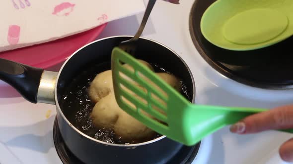 A Woman Fries Dough Donuts In Oil. Turns Over A Donut. Preparing Donuts In The Form Of A Flower