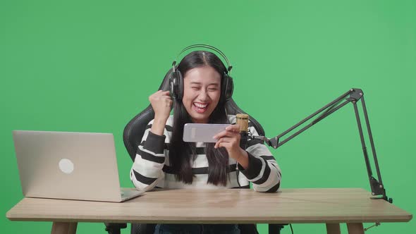 Happy Asian Woman Gamer With Headphone Celebrating Winning The Mobile Phone Game On The Green Screen