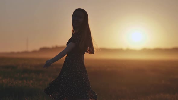 A Silhouette of a Young Girl Dancing and Spinning on a Warm Summer Evening at Sunset
