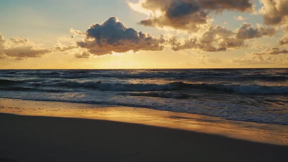 Sunset Behind Clouds Over Sea Waves and Sandy Beach