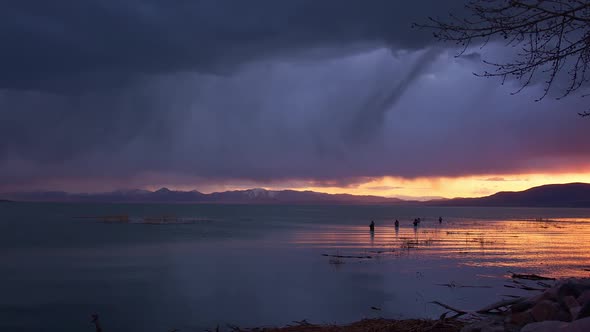 Streaks of rain fall over Utah Lake at dusk past fishermen