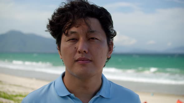 Portrait of a Middleaged Asian Man in a Blue Shirt Standing on the Beach By the Sea Against the