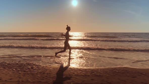 A slender woman runs and jumps on the waves of sea water on a sandy beach.