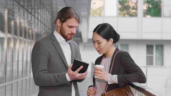 Two Business Colleagues Discussing New Project on Digital Tablet During Coffee Break Outside